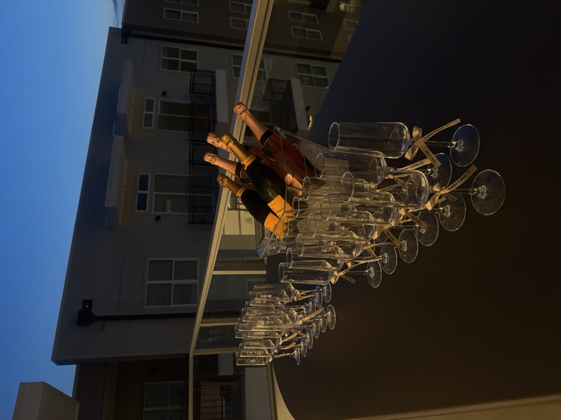 Champagne and rosé bottles chilling in an ice bucket with rows of ribbon-tied flutes on a rooftop terrace at dusk
