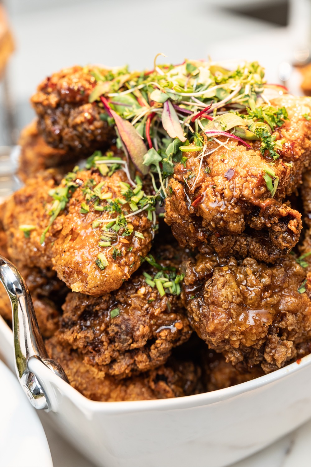 Close-up of crispy honey-glazed fried chicken piled high and topped with microgreens and fresh herbs