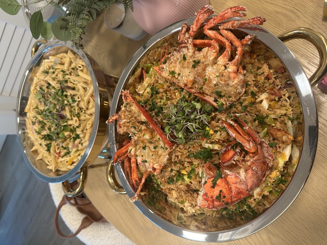 Show-stopping platter of lobster fried rice topped with three stuffed lobsters beside a chafing dish of creamy penne pasta