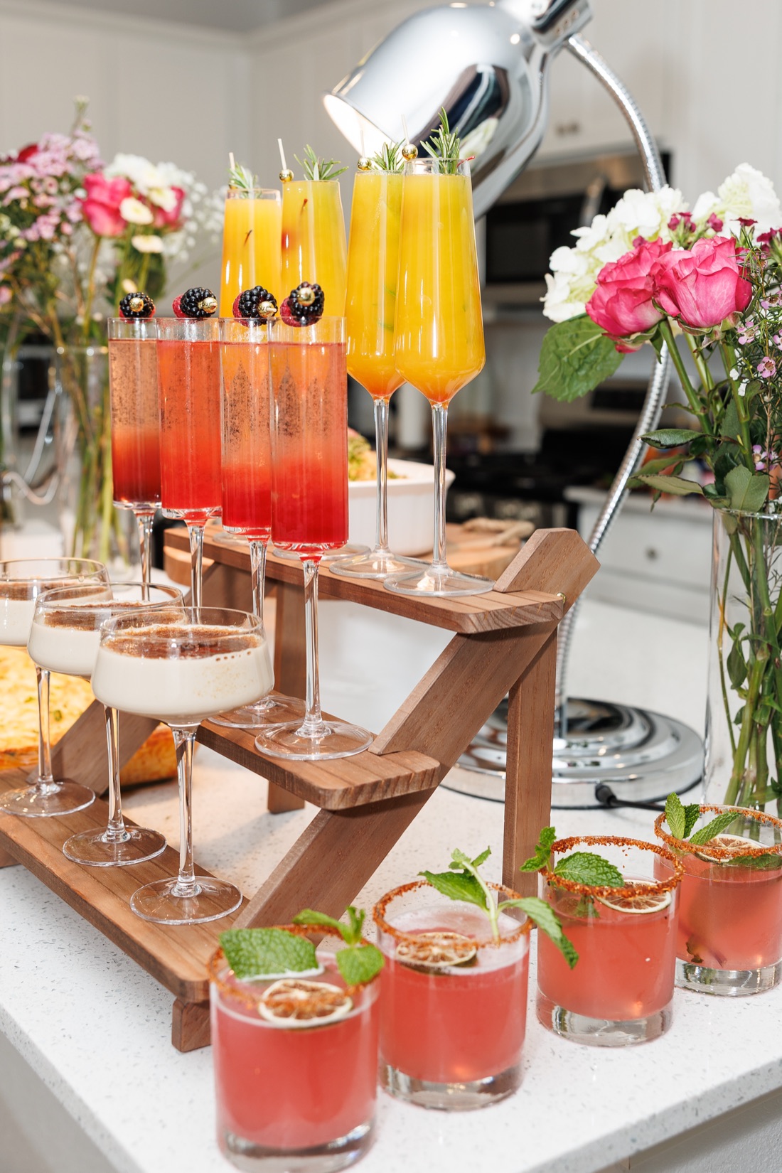 Tiered drink display with berry sunrise bellinis, mango mimosas, crème brûlée coupes, and chili-rimmed margaritas among pink florals