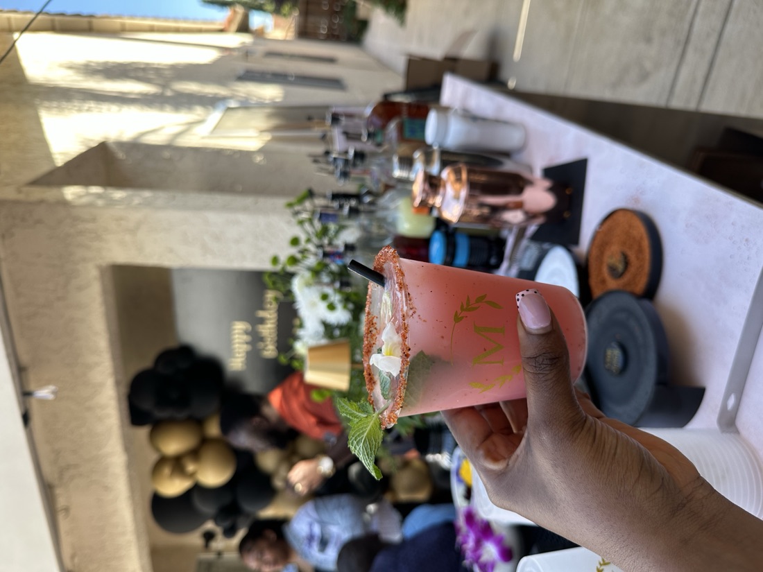 Guest holding a pink craft cocktail with chili-salt rim, fresh mint and edible flower at an outdoor birthday party bar
