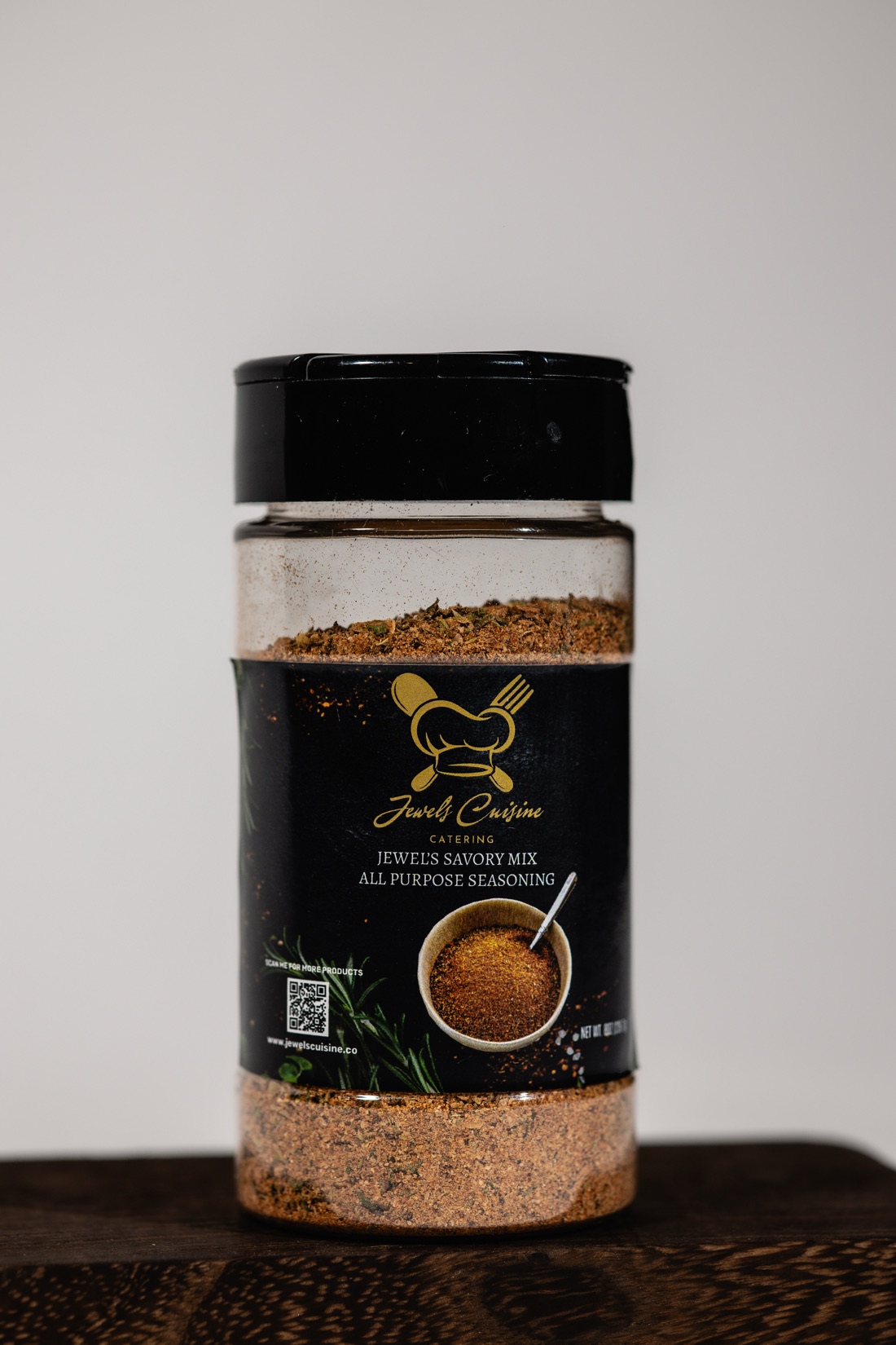 Studio product shot of Jewel's Savory Mix All Purpose Seasoning jar with black and gold Jewel's Cuisine label on dark wood
