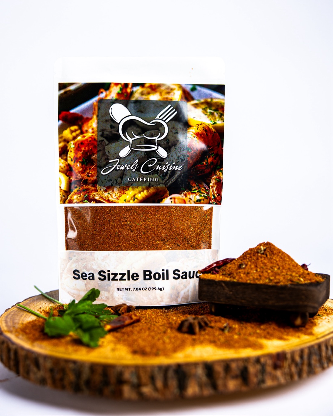 Jewel's Cuisine Sea Sizzle Boil Sauce 7.04 oz seasoning pouch standing on a live-edge wood round with spice mound and fresh parsley