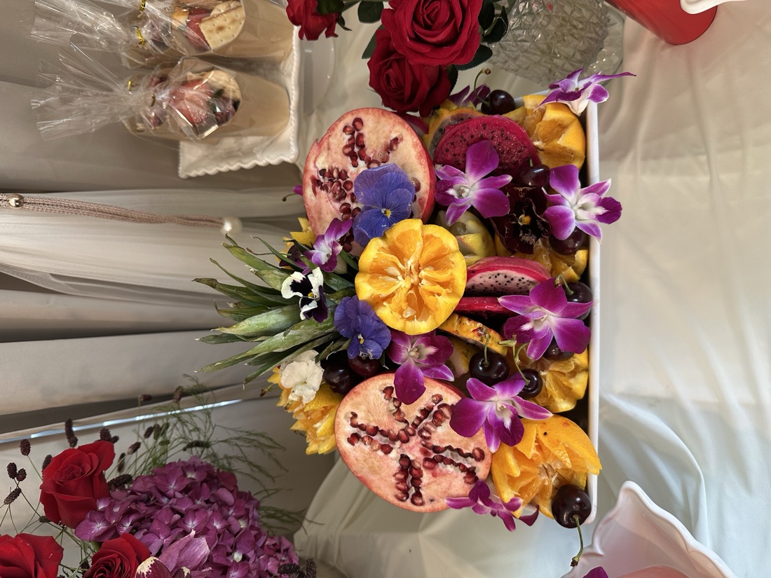 Lavish tropical fruit display with pomegranate halves, oranges, dragon fruit, cherries, and fresh orchids on a white event table